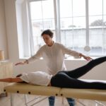 A-Woman-in-White-Top-and-Black-Leggings-Lying-on-a-Massage-Table