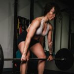 Woman-Leaning-on-Black-Barbell-in-Front-Mirror