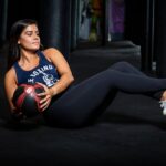Woman-in-Blue-Tank-Top-and-Black-Leggings-Sitting-on-Black-Floor-doing-Russian-Twist