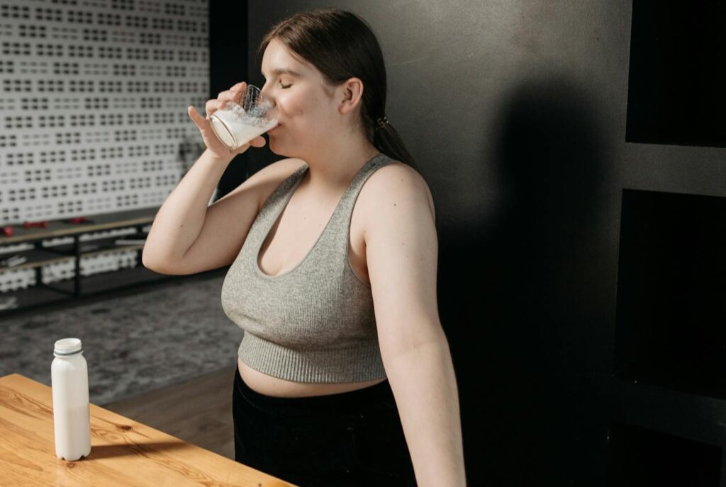 A-Woman-in-Gray-Tank-Top-Drinking-with-Her-Eyes-Closed-while-Standing-Near-the-Wooden-Table