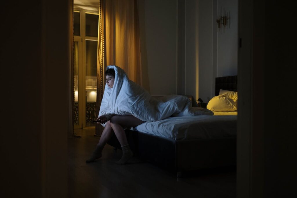 Woman-Sitting-on-the-Bed-while-Covered-by-a-White-Blanket
